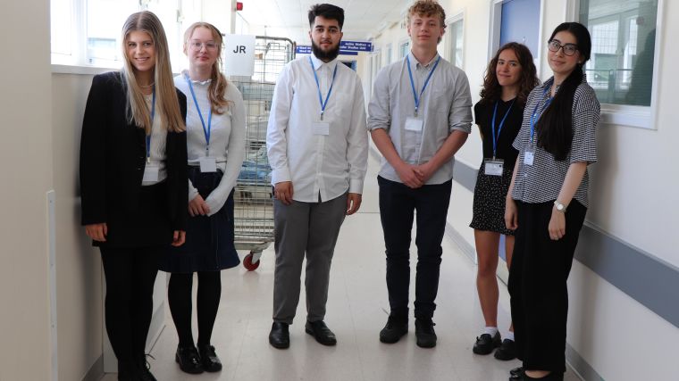 Six work experience students standing in a hospital corridor, smiling at the camera.